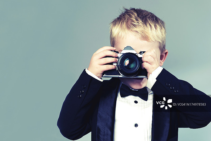 穿着燕尾服的男孩用老式复古相机拍照图片素材