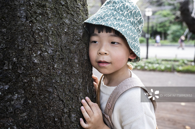 一个神情轻松的男孩把耳朵靠在树干上图片素材