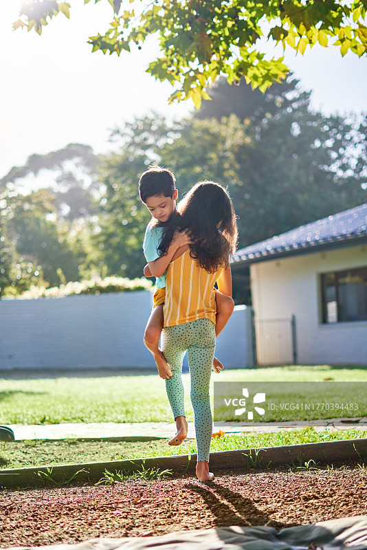 在阳光明媚的夏日后院，妹妹抱着可爱的弟弟图片素材
