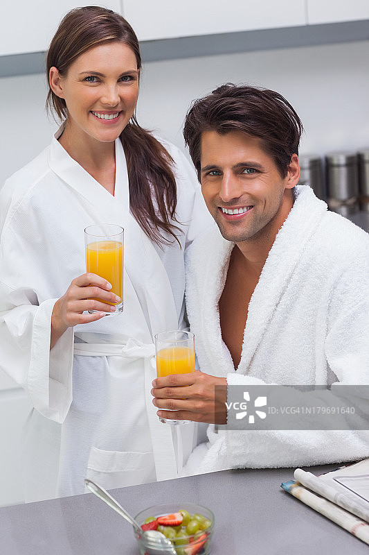 一对可爱的夫妇穿着浴袍，拿着一杯橙汁图片素材
