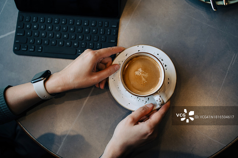 正上方的照片是一个女人在咖啡店里一边喝咖啡一边摆弄她的数码平板电脑。生活方式和科技。灵活的远程工作图片素材