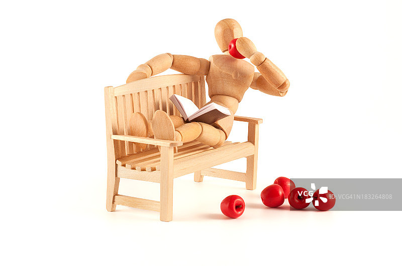 木制人体模型在长凳上休息，吃着苹果图片素材