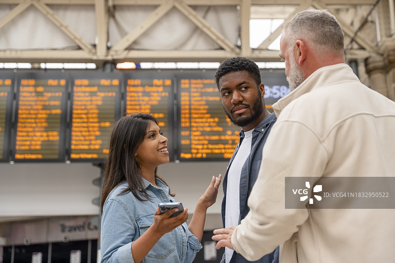 一群不同种族的朋友在火车站登机前在发车板上核对时间。享受火车旅行的概念图片素材