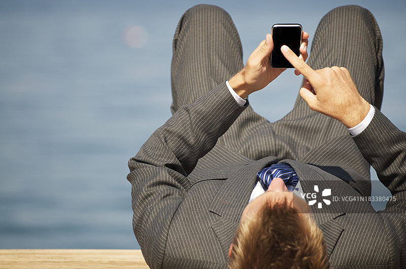 一个穿着西装躺在木头码头上发短信的人图片素材