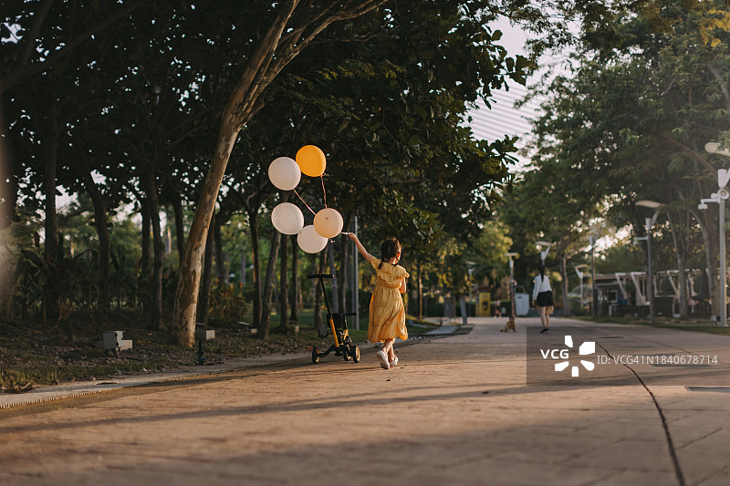 一个亚洲小孩在花园公园里拿着气球跑。库存图片图片素材