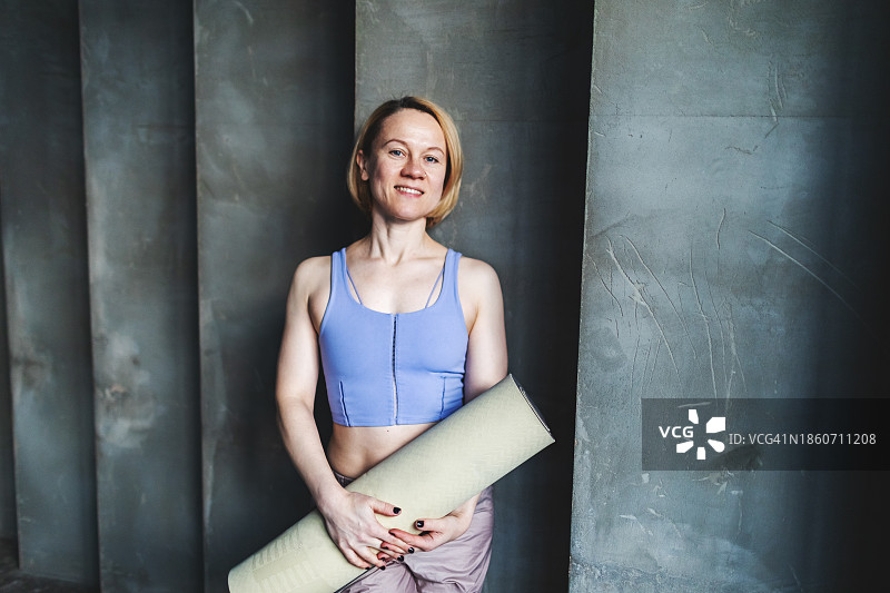 中年成年女性瑜伽教练肖像与运动垫在手中图片素材