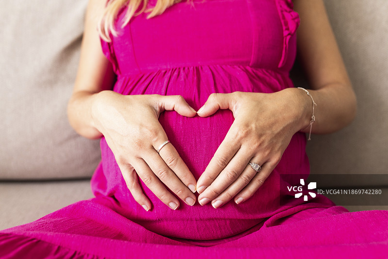孕妇身穿粉色连衣裙，在肚子上做心形手势图片素材