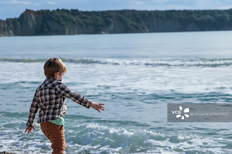 快乐的小男孩(3-4岁)穿着棕色格子衬衫在海边玩耍。图片素材