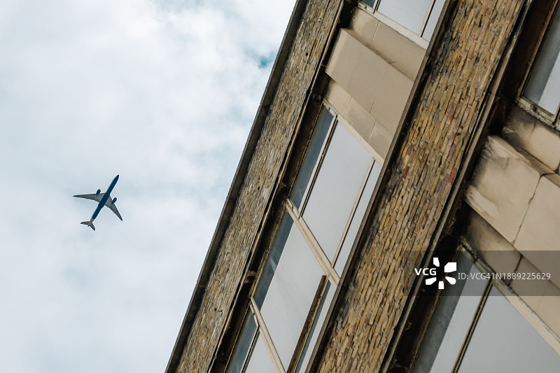 商用飞机在伦敦摩天大楼上空飞行的低角度视角。图片素材
