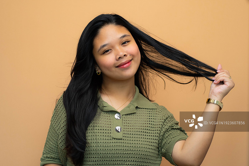 一个俏皮的年轻东南亚女人的头像，黑色波浪发型在棕色背景上图片素材