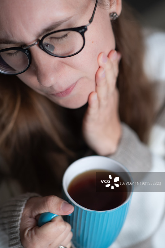 喝着热茶的女人正在遭受牙齿敏感的折磨图片素材