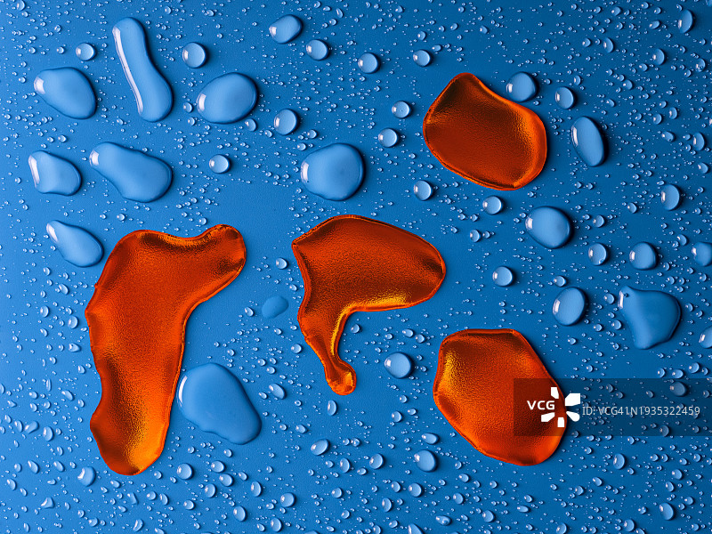 红色金属液滴与小水滴一起在潮湿的蓝色背景上滑动。图片素材
