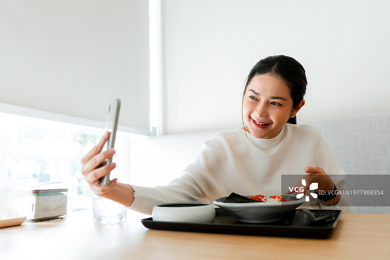 一名女子在餐厅享受美食，并在社交媒体上自拍图片素材