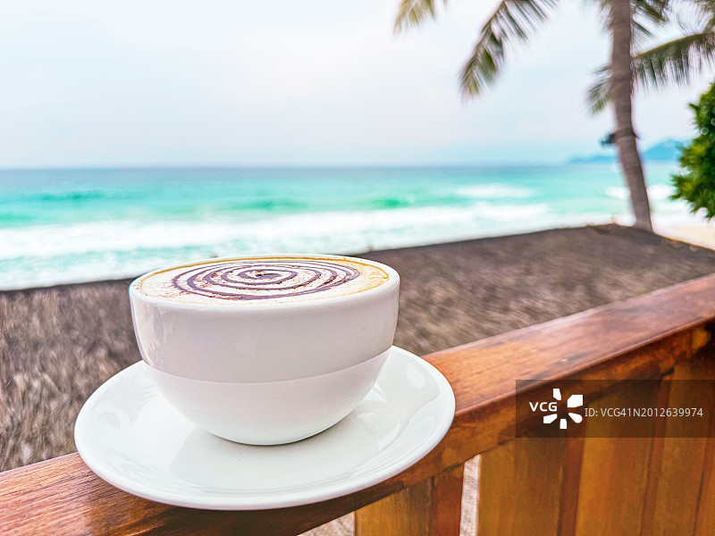 白杯咖啡卡布奇诺在热带海滩与棕榈树的背景。图片素材
