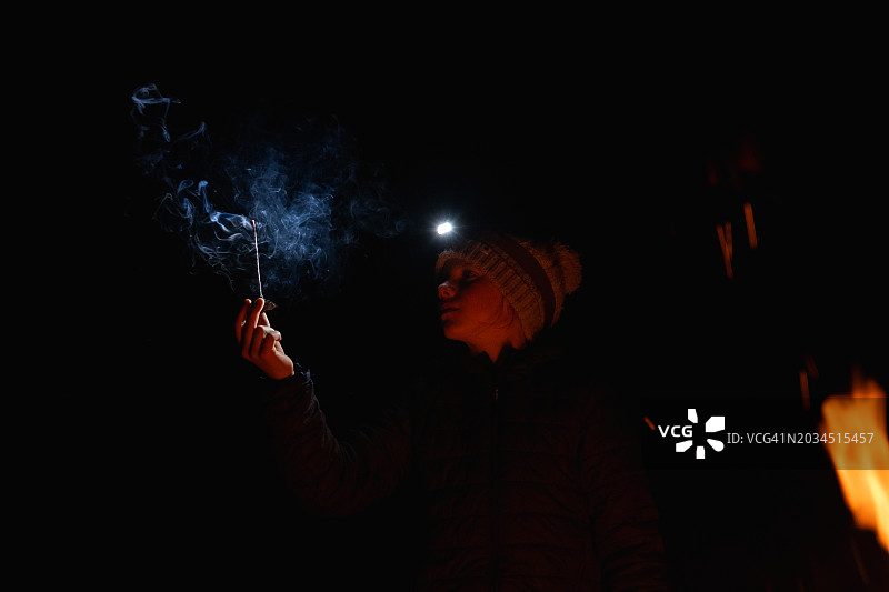 年轻的女孩在晚上用一根燃烧的棍子制作烟雾图案图片素材