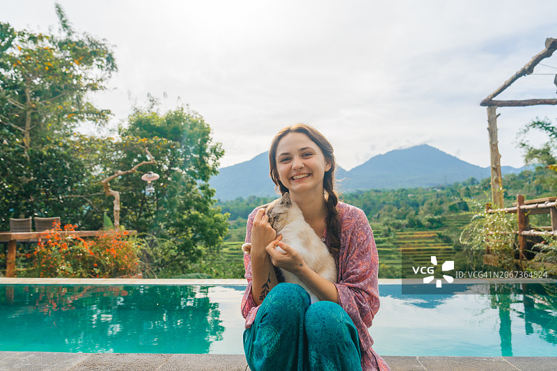 巴厘岛，一个女人和她的猫坐在泳池边图片素材