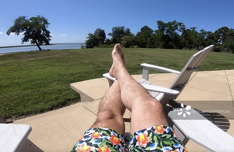 一个男人在他的后院休息，穿着短裤，放松地晒着日光浴，看着大海。图片素材