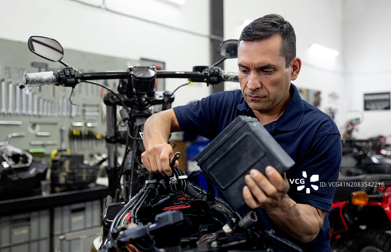 汽车修理店的机械师正在给摩托车接上电池图片素材