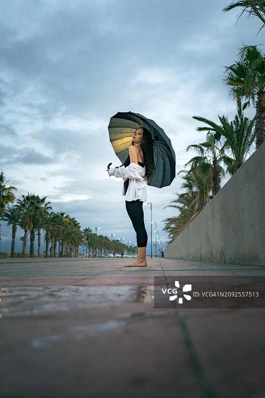 一个赤脚的舞者在下雨天打着伞摆出惊人的舞蹈姿势。图片素材