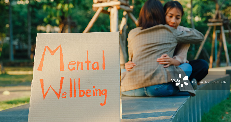 特写:在一场心理健康意识活动中，两名年轻的亚洲女性在公园里相互拥抱，强调同情和关怀。户外心理健康社区支持。图片素材