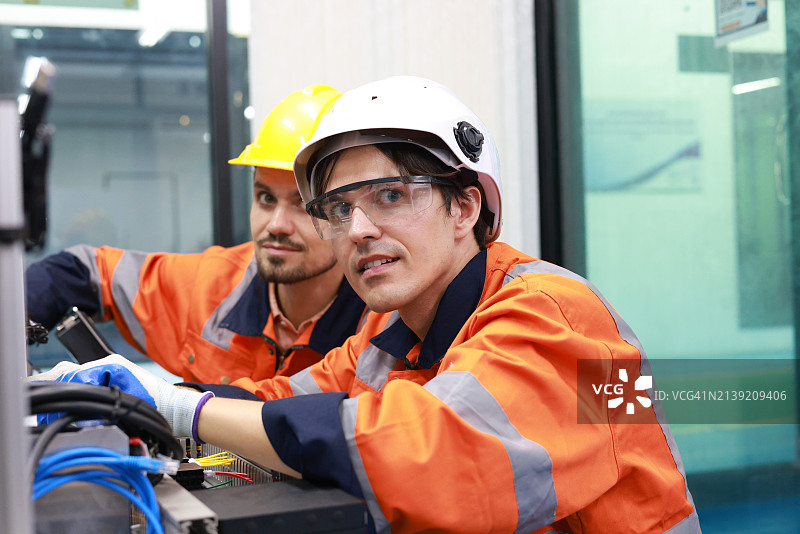 两名熟练的机电工程师，配备安全PPE，正在工厂勤奋地进行维护和配置先进的自动化系统。图片素材