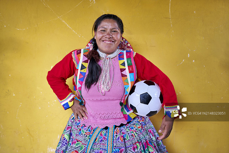 一幅黄色背景的克丘亚族女足球运动员的肖像，她手里拿着球，面带微笑图片素材