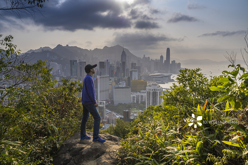 亚洲人站在岩石上看香港的天际线，日落图片素材