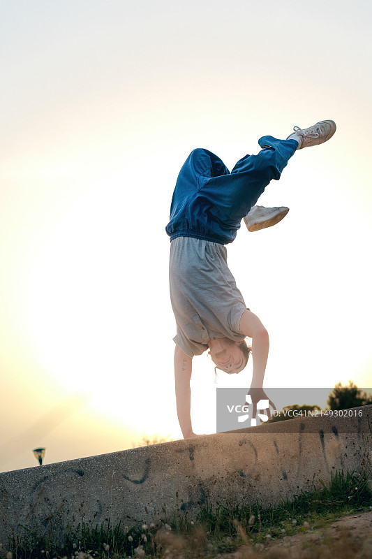 一个年轻人在日落时分表演杂技，一个扎着马尾辫的男孩在公园里跳着舞。图片素材