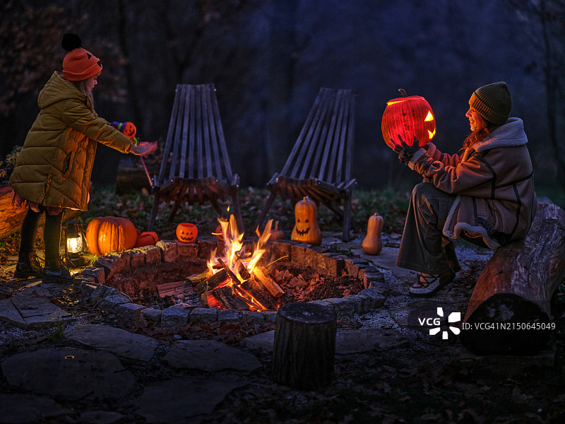 万圣节晚上，快乐的母女在篝火旁。图片素材