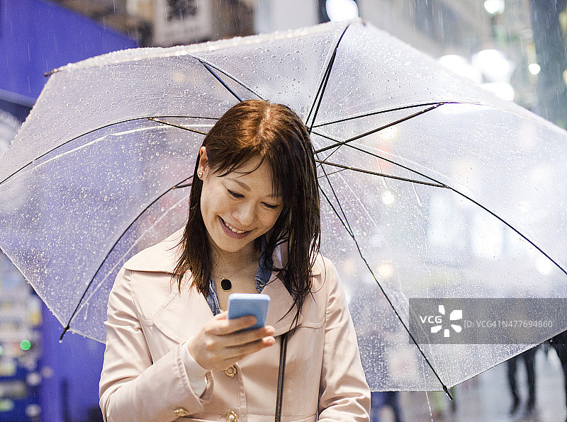 带着雨伞微笑的日本女子在东京发短信图片素材