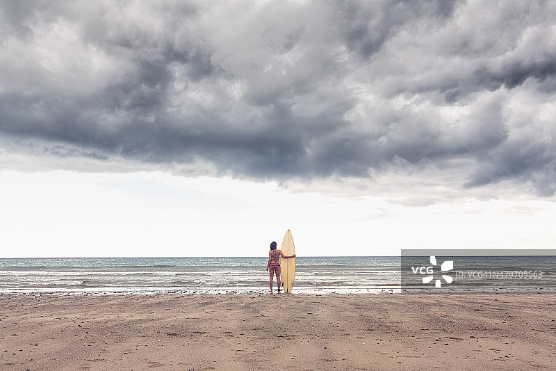 平静的女人在海滩上穿着比基尼和冲浪板图片素材