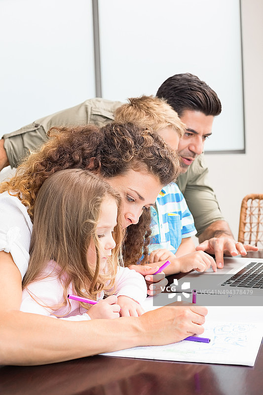 有吸引力的父母与他们的孩子着色和使用笔记本电脑图片素材