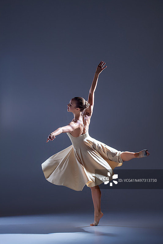 年轻美丽的舞者在米色连衣裙上跳舞在灰色的背景图片素材