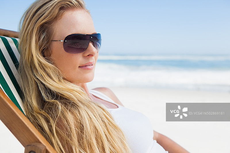 漂亮的金发美女戴着墨镜坐在海滩上图片素材