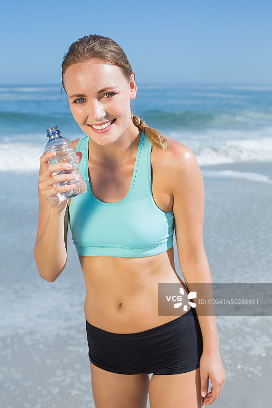 健康的女人站在沙滩上喝酒图片素材