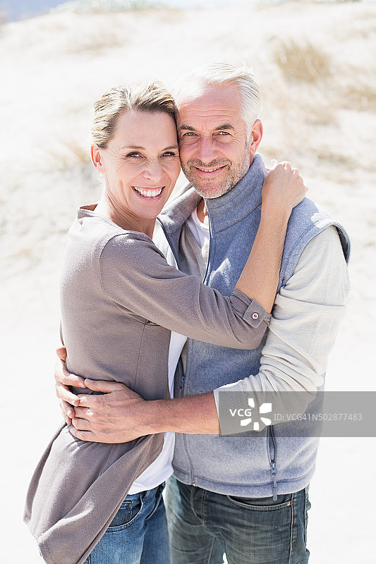 一对快乐的情侣在沙滩上看着镜头拥抱图片素材