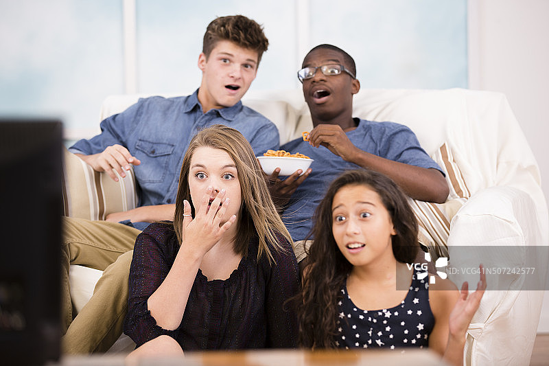 青少年一起在家里的家庭活动室看电视。惊喜。图片素材