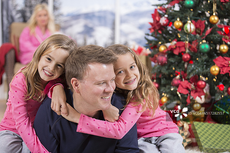 女儿们在圣诞节的早晨拥抱父亲。家庭。树妈妈的背景。图片素材