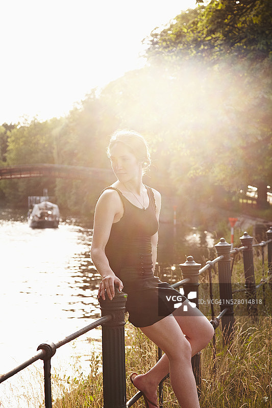 日落时分，一个年轻女子靠在运河附近的栏杆上图片素材