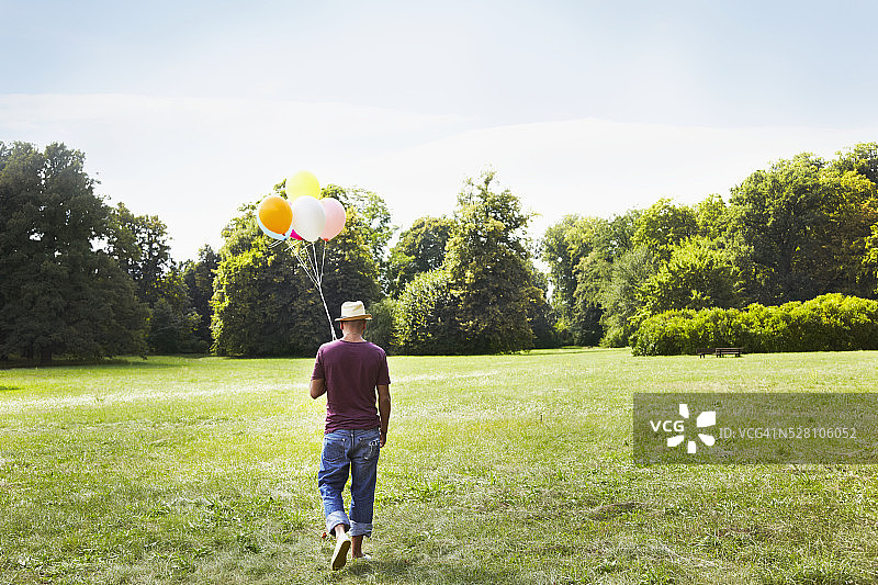 一个人在草地上走着，手里拿着一堆彩色的气球图片素材