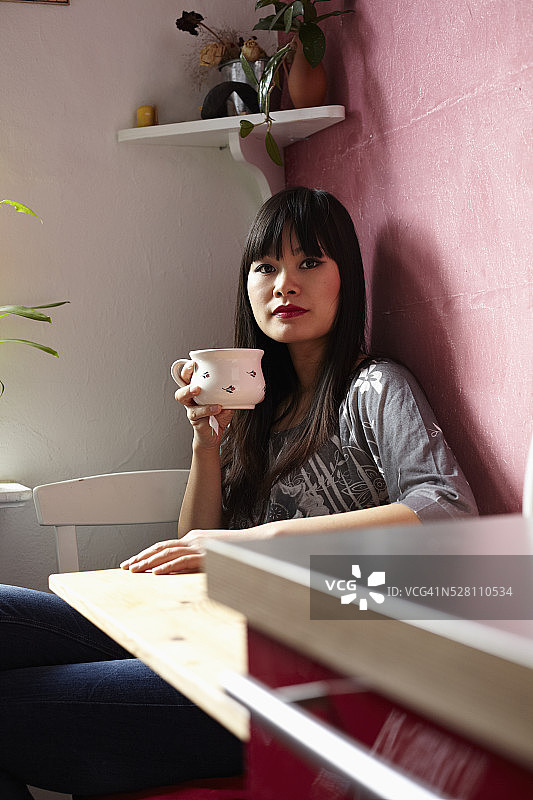 年轻的中国女人坐在厨房里喝茶图片素材