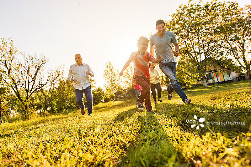 快乐的小男孩和他的家人在草地上跑步。图片素材
