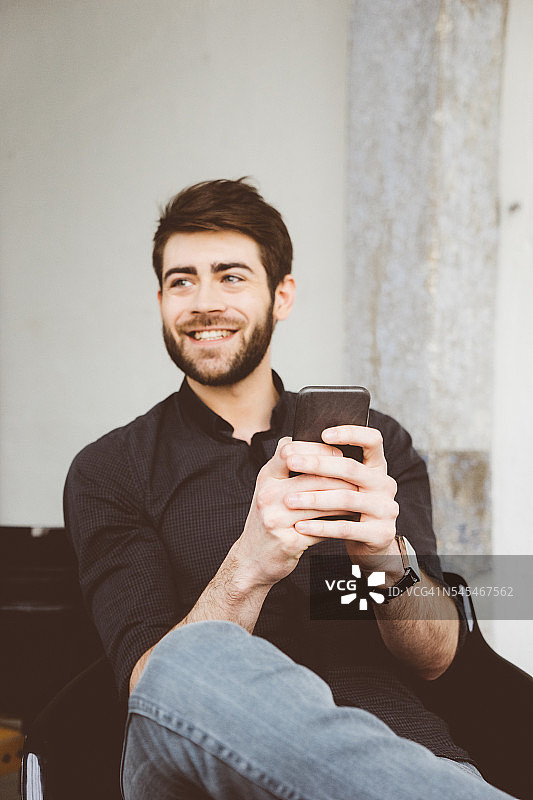 一个快乐的年轻人用他的智能手机给朋友发短信图片素材