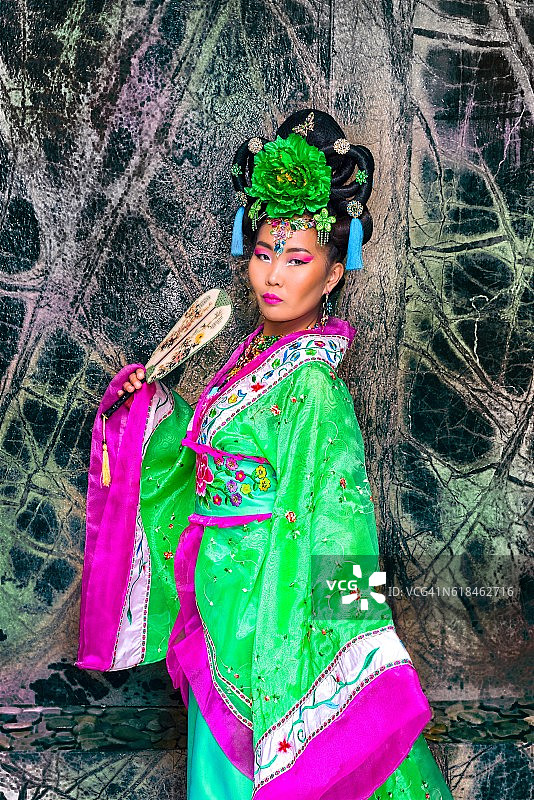 美丽的亚洲女子穿着中国服装，手持传统扇子图片素材