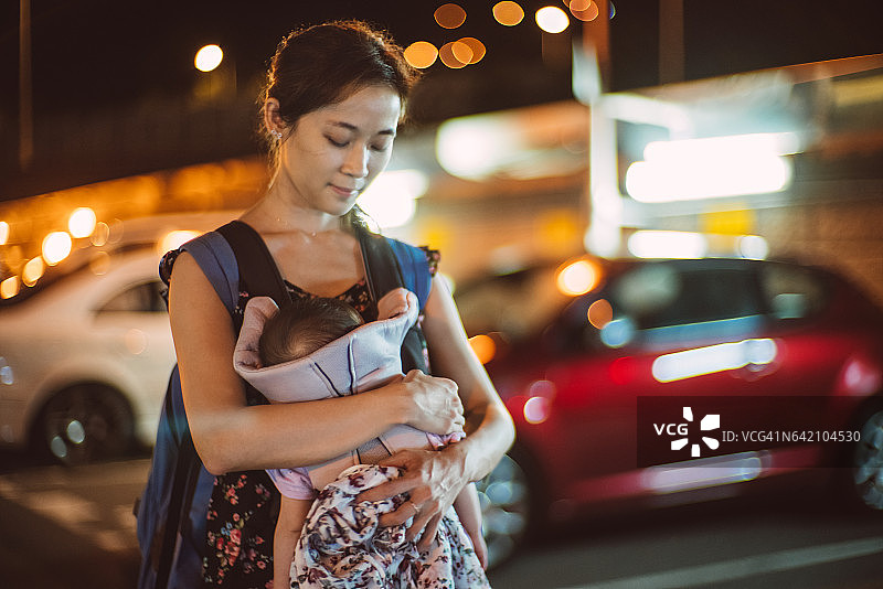 年轻漂亮的妈妈晚上抱着熟睡的孩子在停车场里图片素材