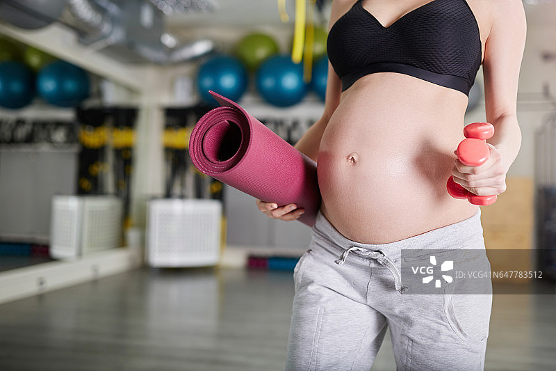 孕妇在健身房举着杠铃和垫子图片素材