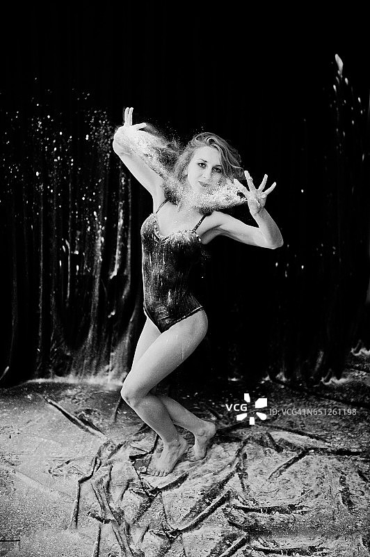 女孩舞者在白色的灰尘和面粉在黑色的背景跳舞。一名女子在面粉上跳舞。图片素材
