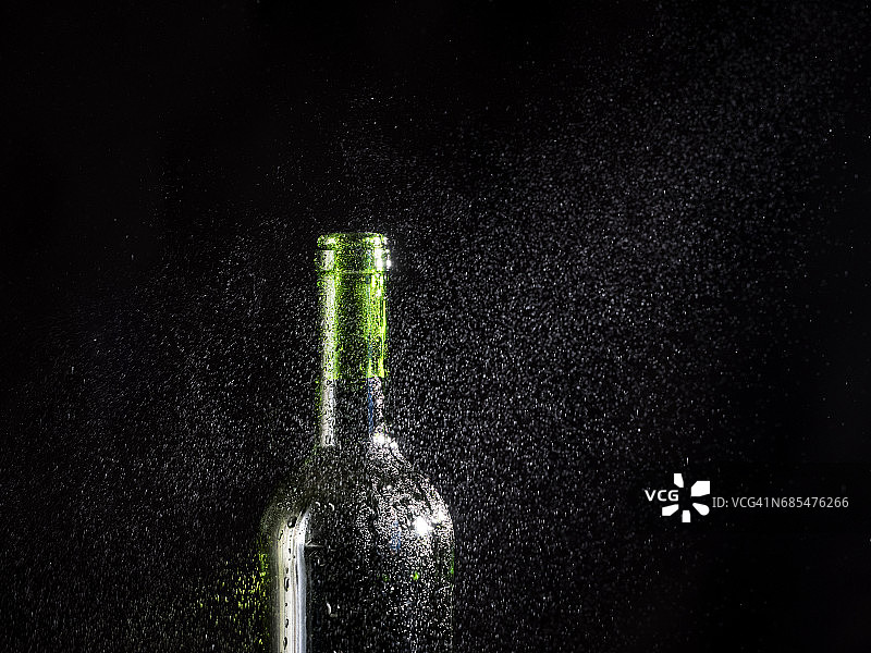 一瓶啤酒，配上磨砂玻璃杯，上面有水滴和一团凝结在黑色底部的蒸汽云图片素材