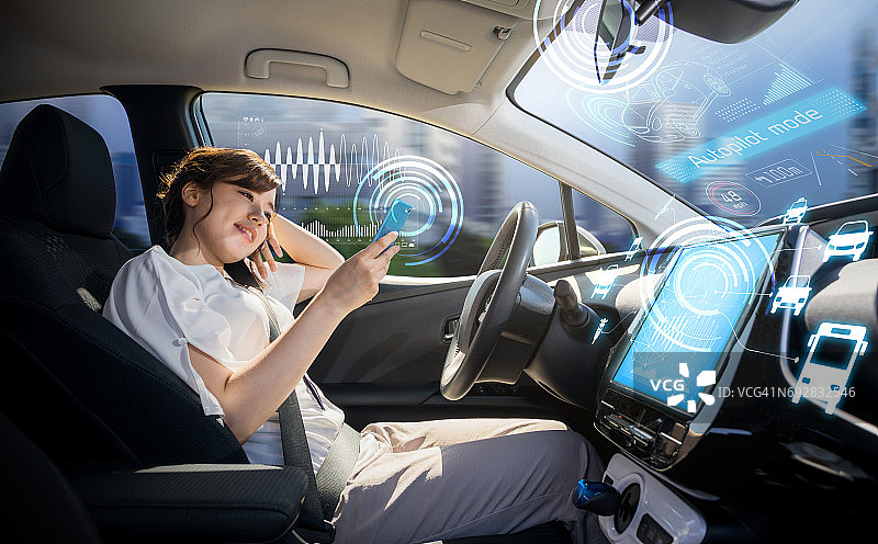 女性在自动驾驶汽车上使用智能手机。自己驾驶车辆。自动驾驶仪。汽车技术。图片素材