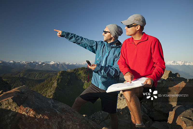 两名男子在野外徒步旅行时，使用纸质地图和指南针来识别附近的山峰。图片素材